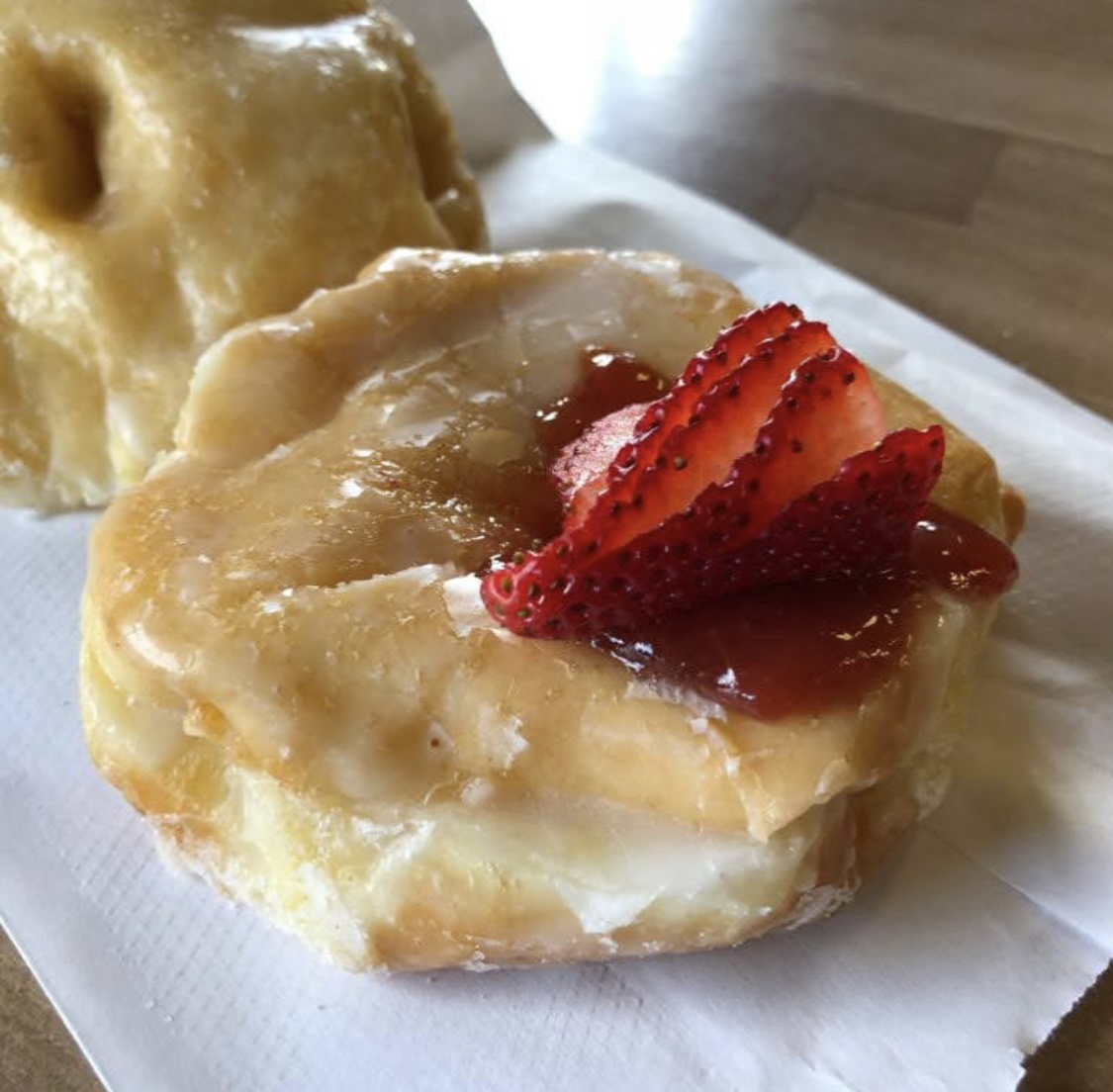 Close up of a glazed donut topped with fresh strawberry and jam